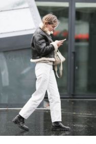 White jeans styled with a black leather jacket, beige knit and black boots