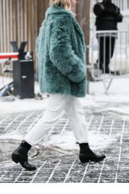 White jeans styled with a teal coat and black boots