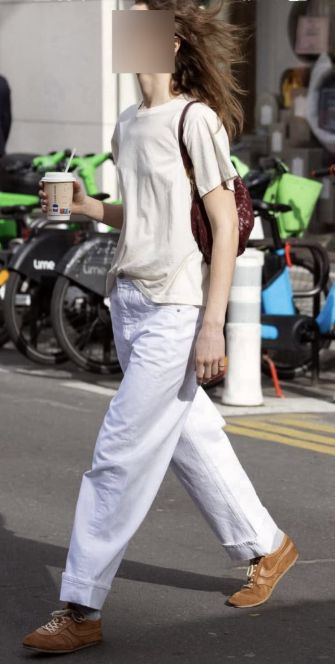 A casual womenswear outfit with a cream T-shirt, white wide-leg jeans, tan trainers, sunglasses and a burgundy bag